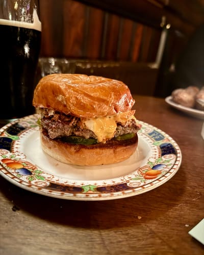 Glossy-bunned Dexter Cheeseburger with melted cheese and pickles on a vintage floral plate at The Plimsoll